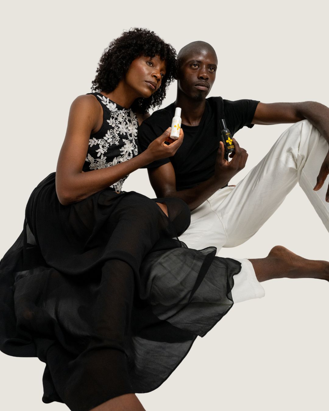Two people sitting together on a white surface, one holding a bottle.